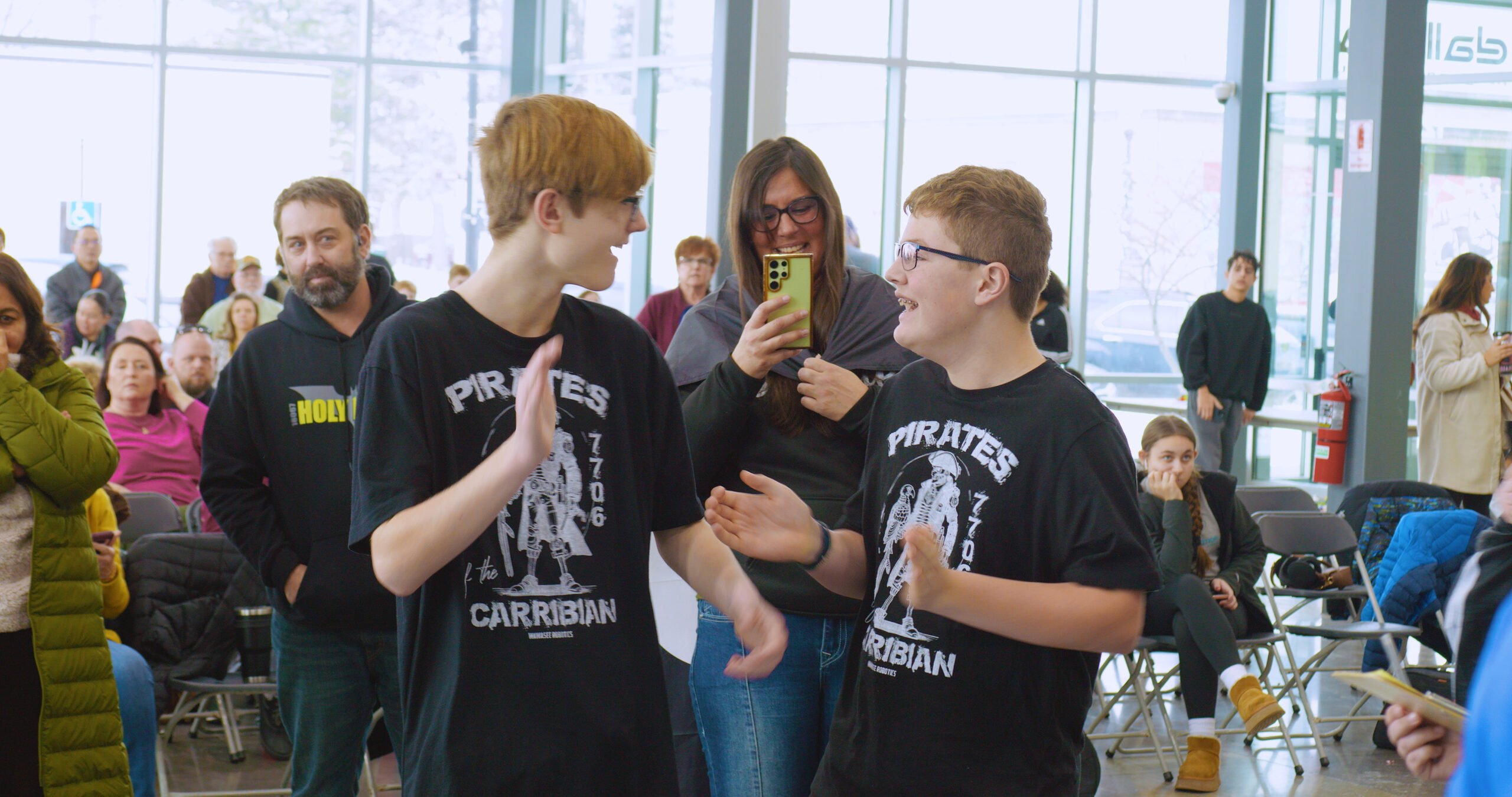 Two Boys smiling and clapping while a parent uses phone to record.